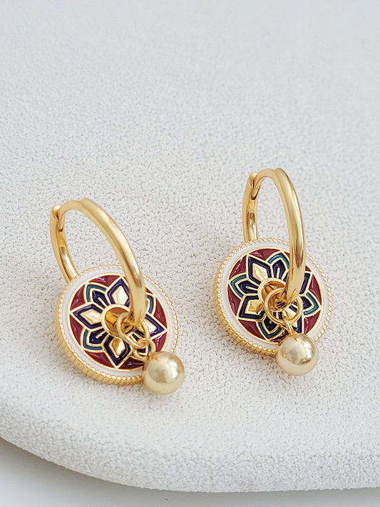 Gold hoop earrings featuring a tile pattern disc and a gold ball dangle, displayed on a white surface showcasing their elegant and unique artisan design.