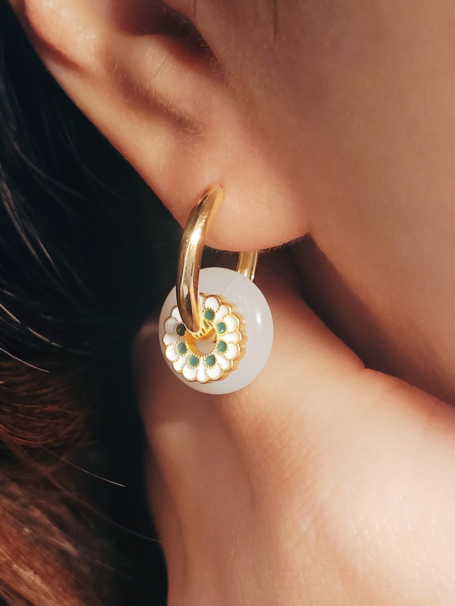 A woman elegantly showcases her gold and white enamel drop hoop earrings, exuding sophistication and style. Inspired by the art of ceramic tile patter, crafted in yellow gold vermeil and enmel. 