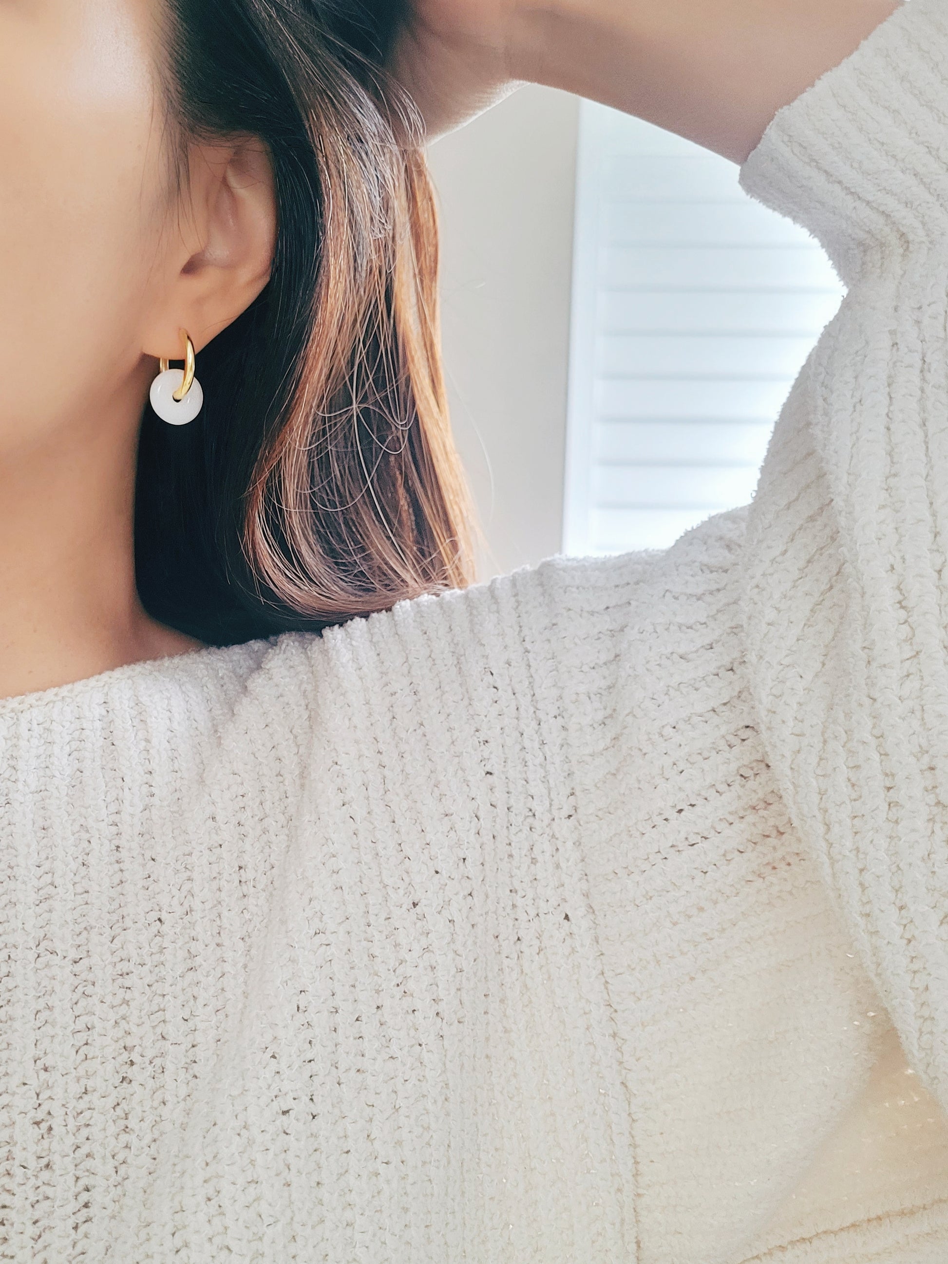 A woman elegantly showcases her gold hoop earrings, complemented by the exquisite Snowy White Drop design.