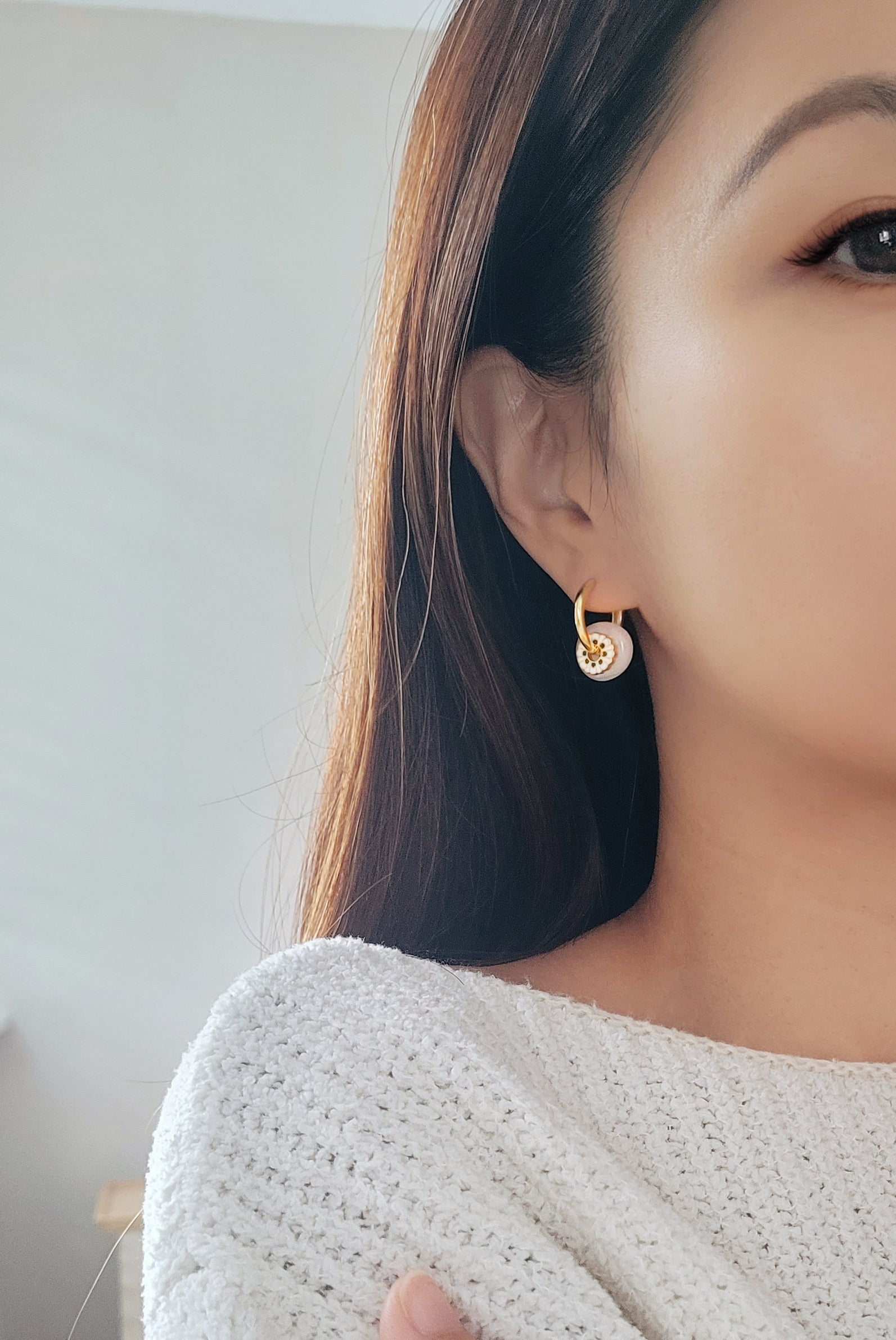 A woman flaunts her stunning gold and white jade enamel drop hoop earrings, embodying elegance and refined taste.