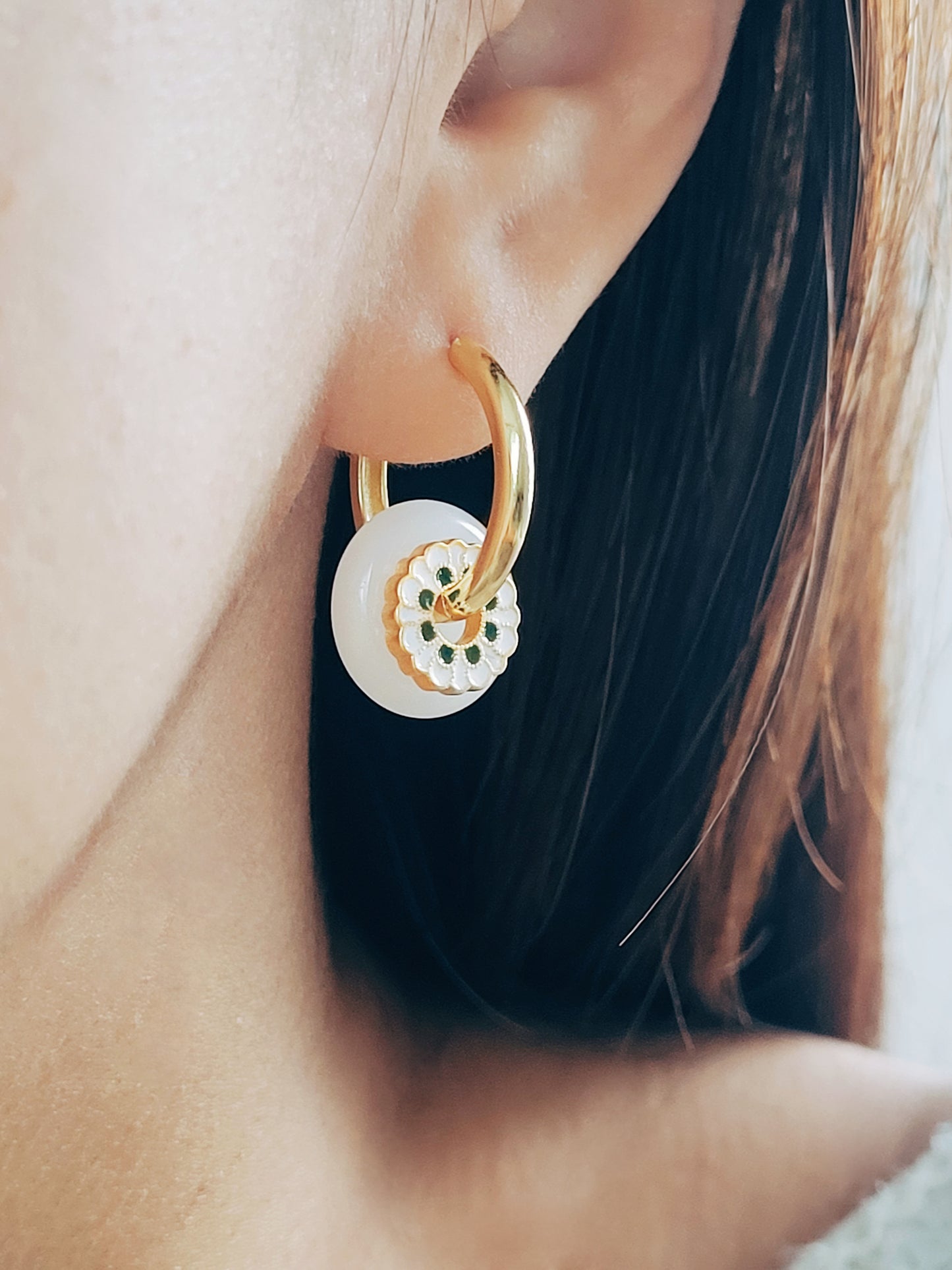 A stylish woman adorned with gold hoop earrings, featuring the luxurious Enamel Flower disc and snowy White Drop detail for a chic touch.