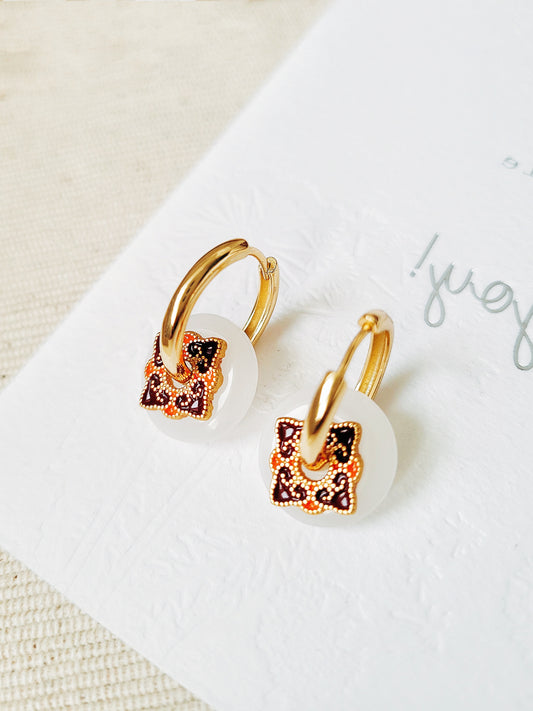 Close-up of enamel hoop earrings with white dangle and vintage tile-inspired charm, set against a neutral background.