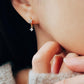 Model wearing a gold flower huggie earring with a dangling cubic zirconia stone, showing a dainty and elegant fit.