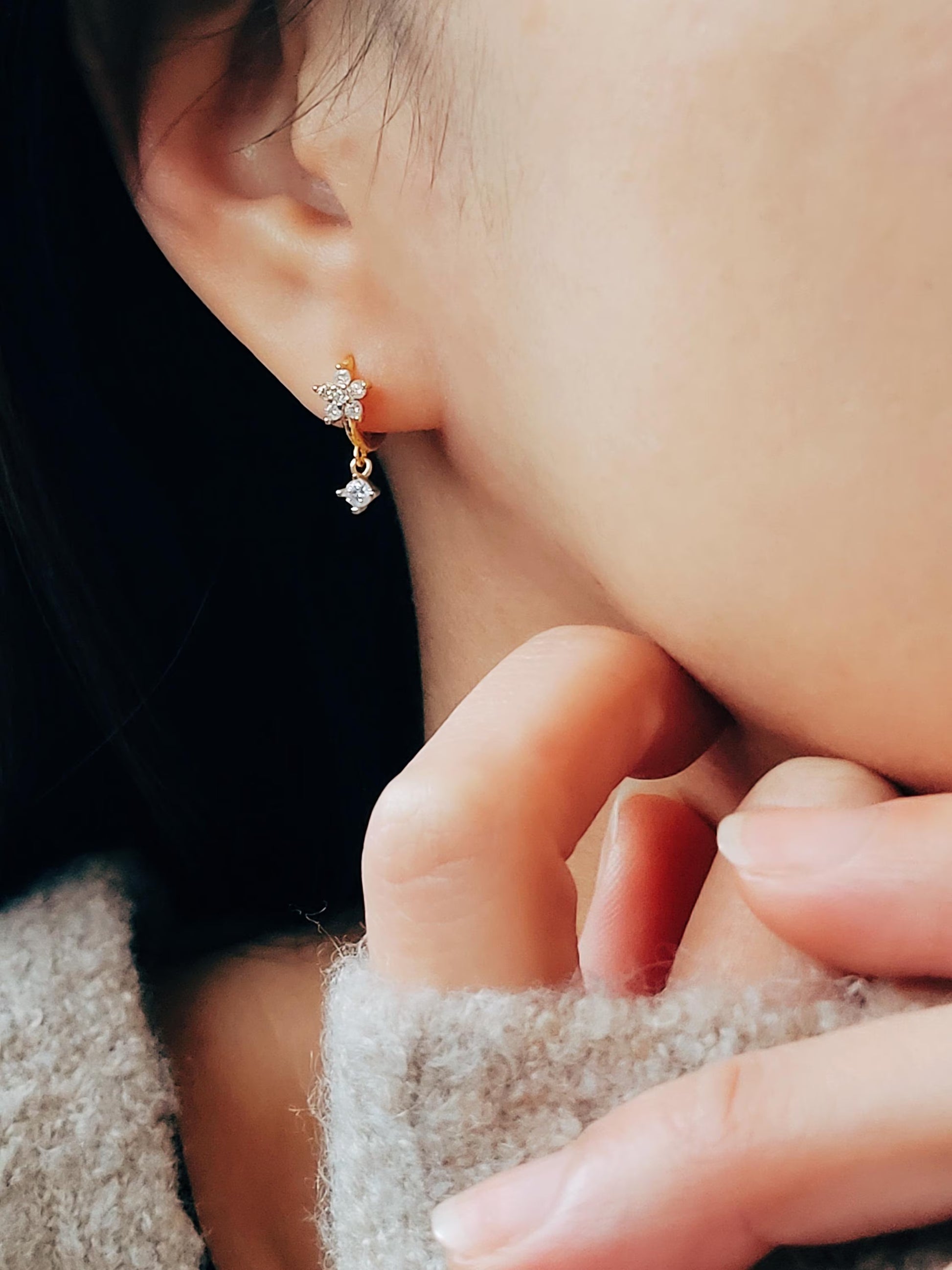Model wearing a gold flower huggie earring with a dangling cubic zirconia stone, showing a dainty and elegant fit.