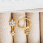 Gold-plated earrings with cubic zirconia stones on a textured beige surface.