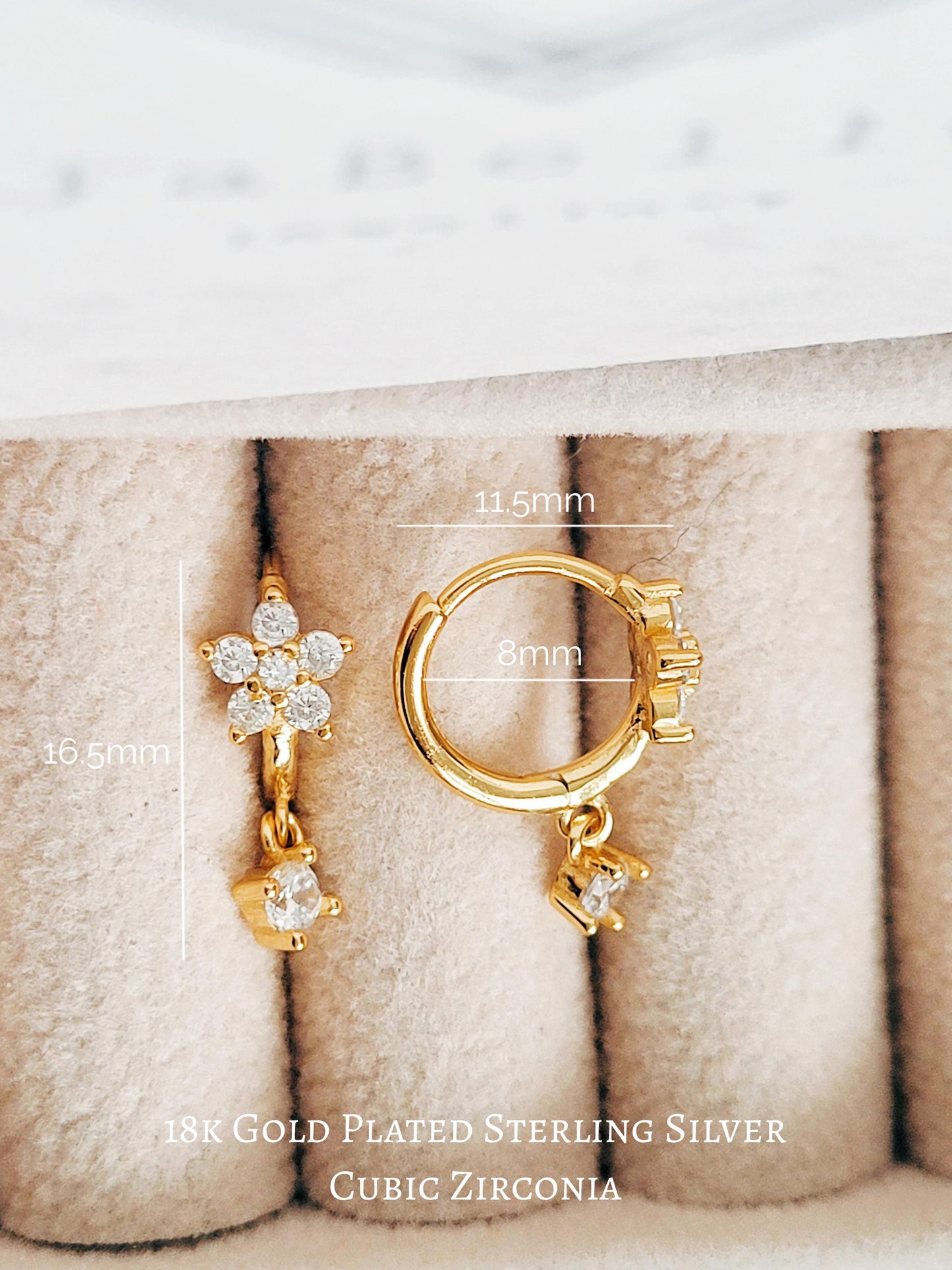 Gold-plated earrings with cubic zirconia stones on a textured beige surface.