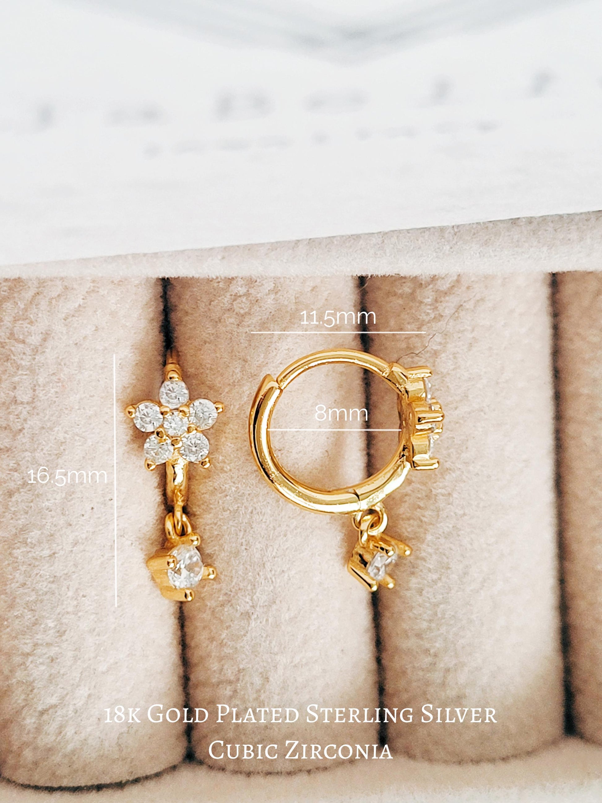 Gold-plated earrings with cubic zirconia stones on a textured beige surface.