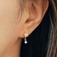 Close-up of a woman wearing dainty flower huggie earrings with a small dangle, elegant jewellery gift for her.
