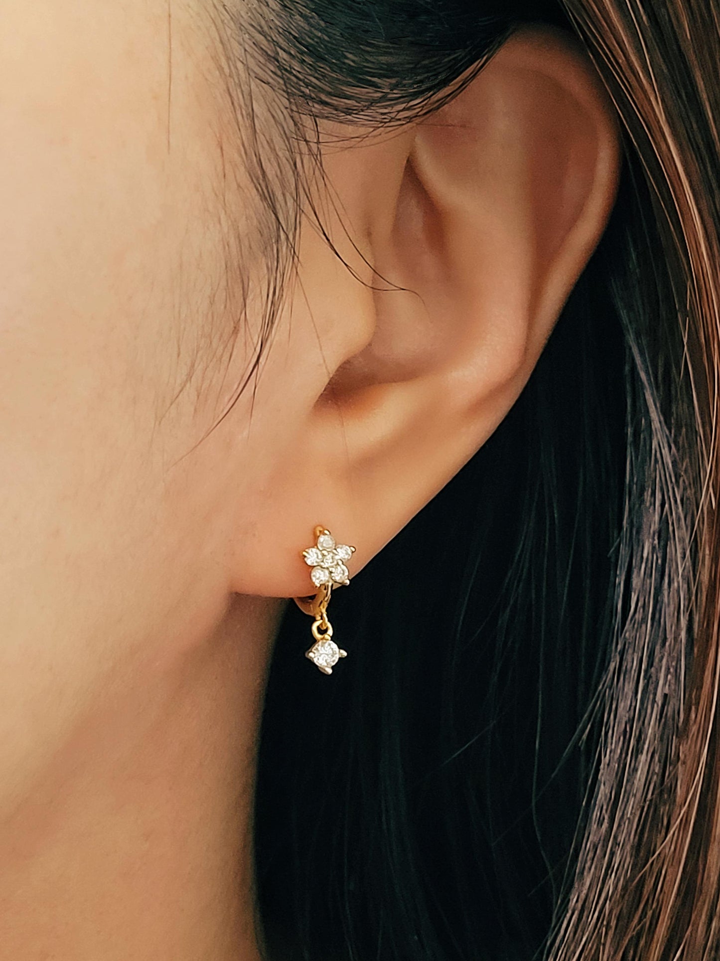 Close-up of a woman wearing dainty flower huggie earrings with a small dangle, elegant jewellery gift for her.