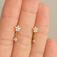 Gold flower earrings with small diamonds held between fingers against a neutral background