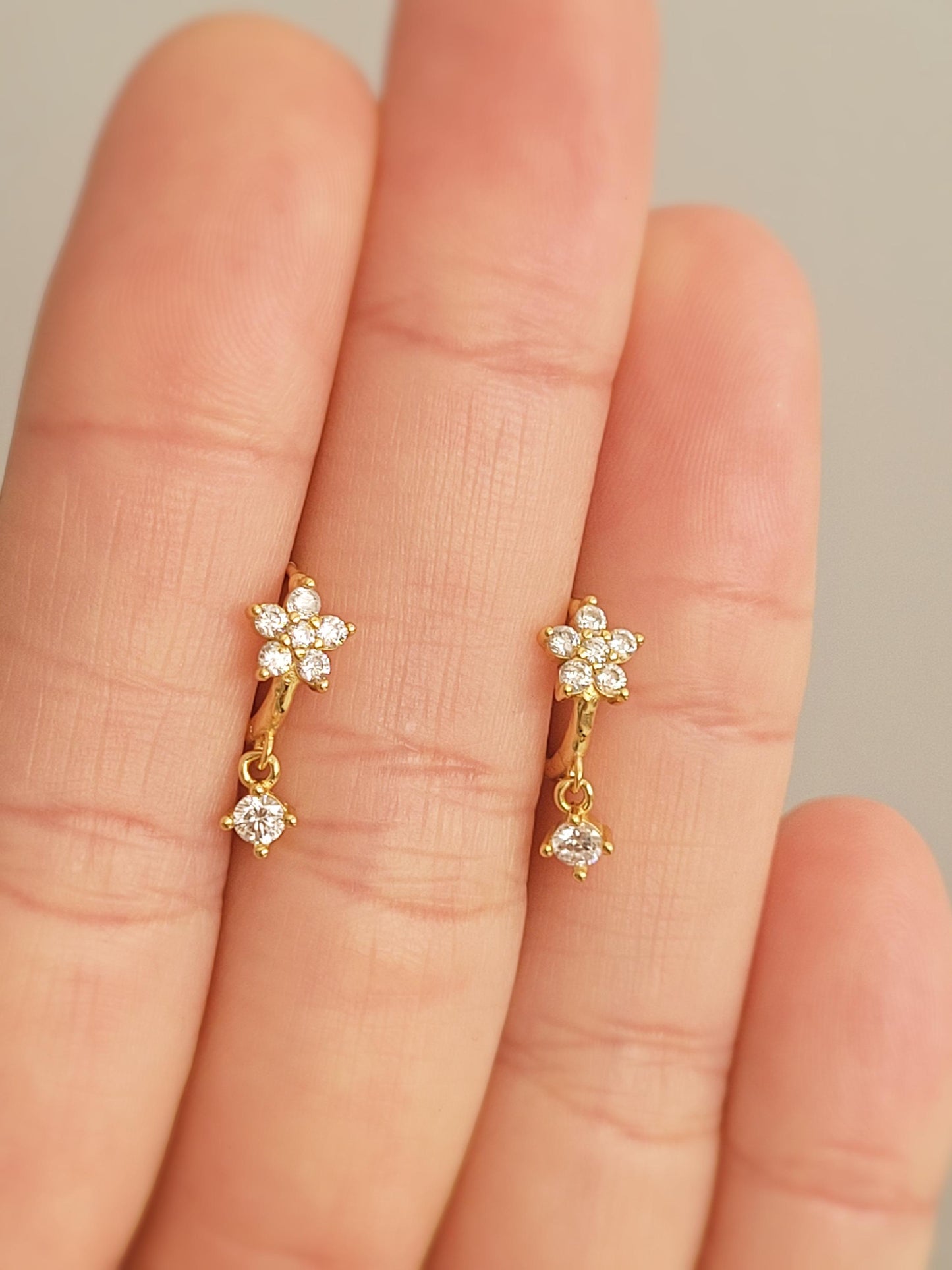 Gold flower earrings with small diamonds held between fingers against a neutral background