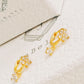 Gold flower huggie earrings with clear stones on a textured white surface