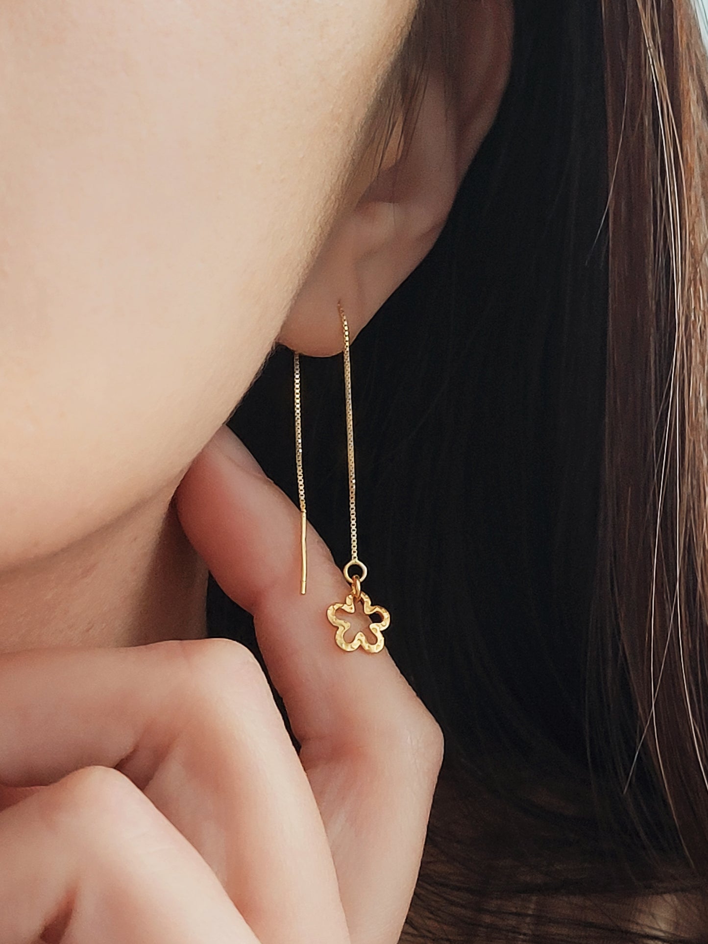 Gold flower-shaped earring worn by a woman with dark hair.