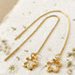 Gold flower earrings crafted in gold plated sterling silver on a textured beige surface with dried flowers.