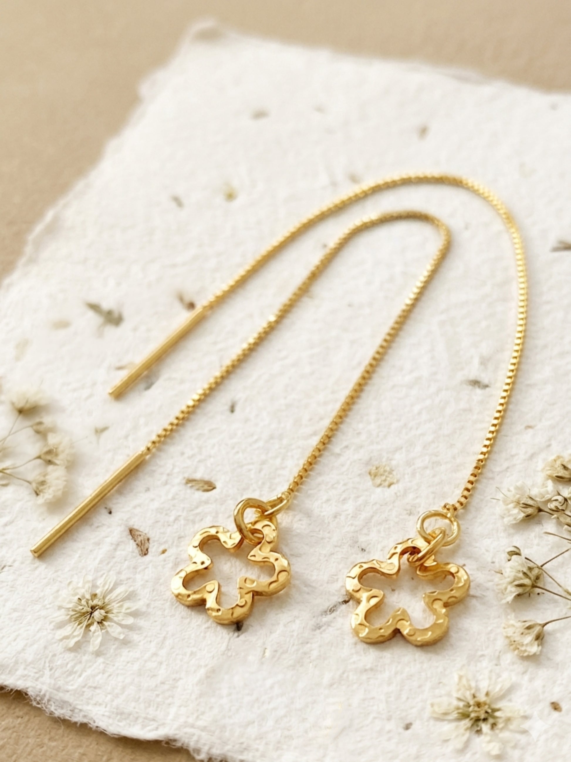 Gold flower earrings crafted in gold plated sterling silver on a textured beige surface with dried flowers.