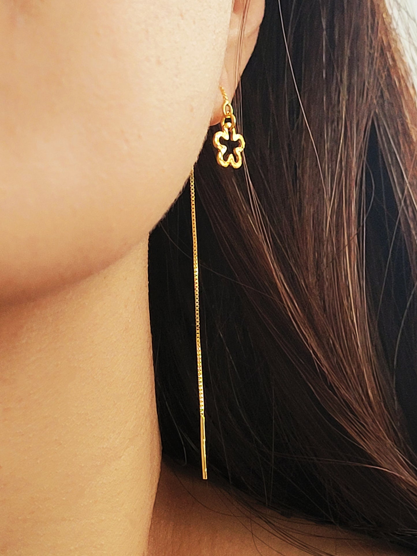 Gold threader pull through earring in gold worn by a woman with long dark hair.