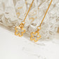 Gold long chain earrings with floral pendants on a textured glass surface