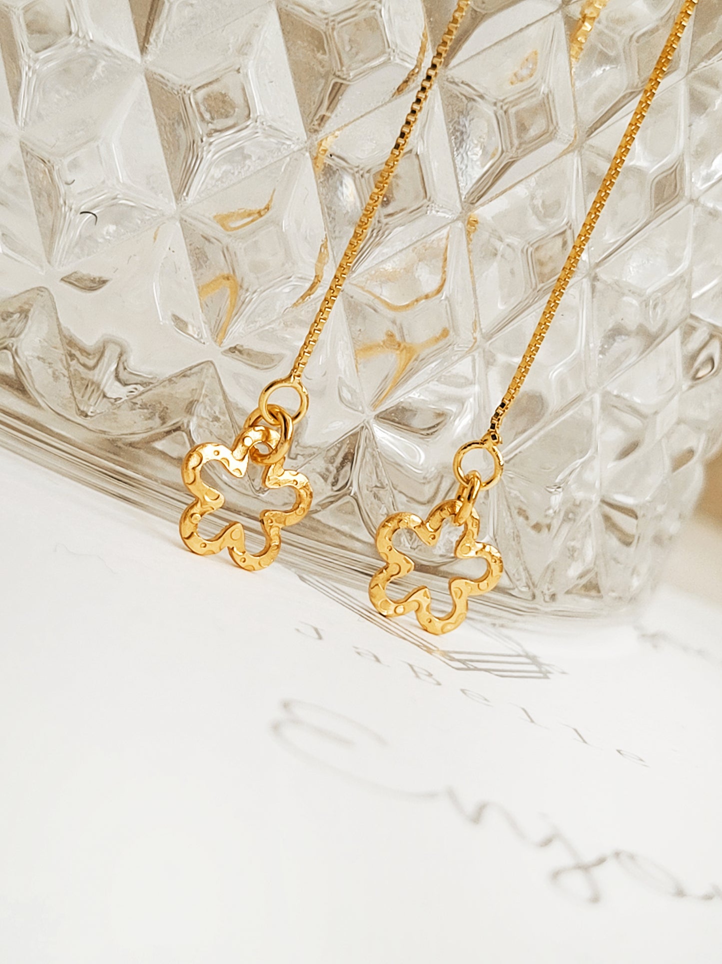 Gold long chain earrings with floral pendants on a textured glass surface
