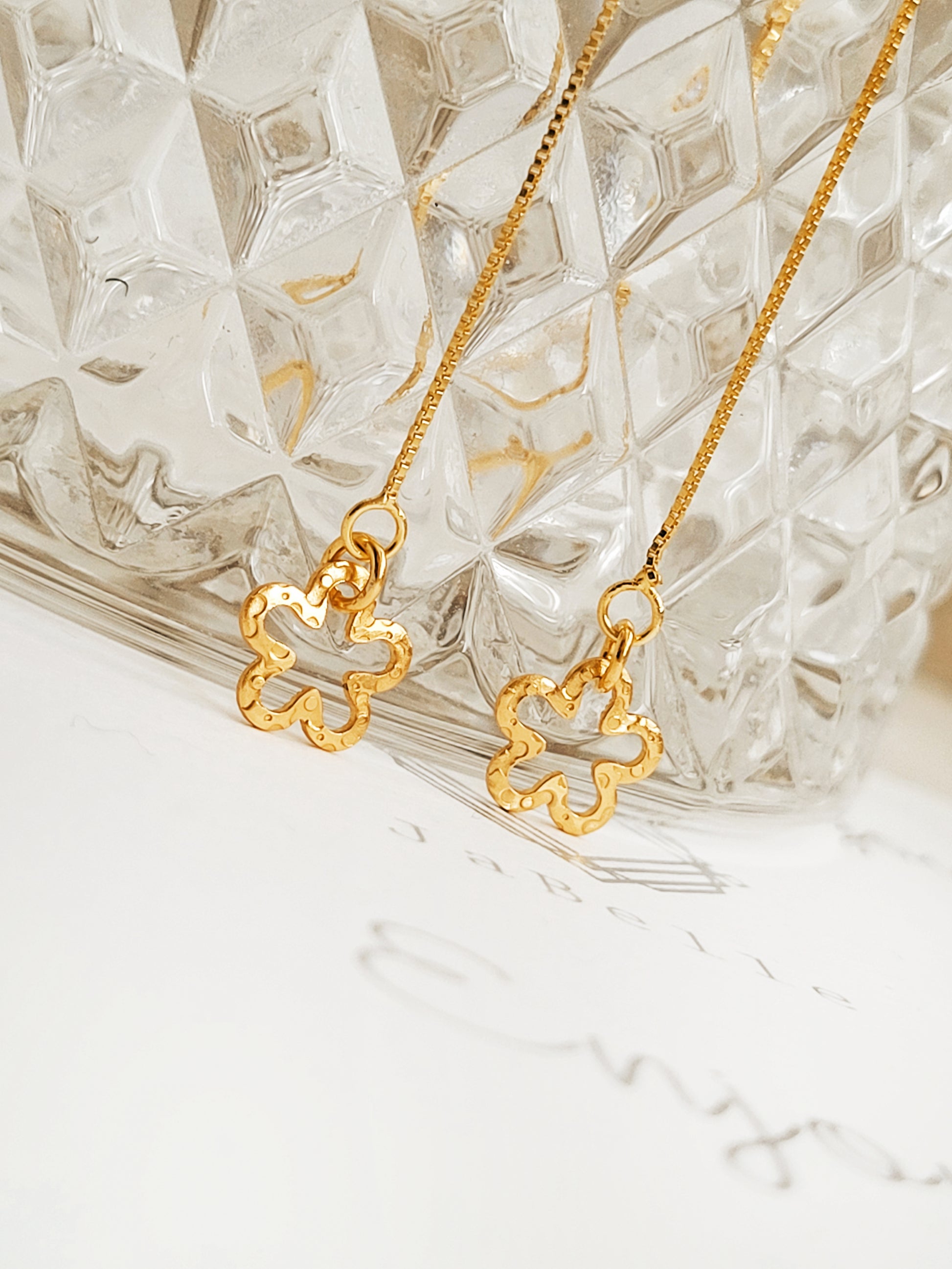 Gold long chain earrings with floral pendants on a textured glass surface