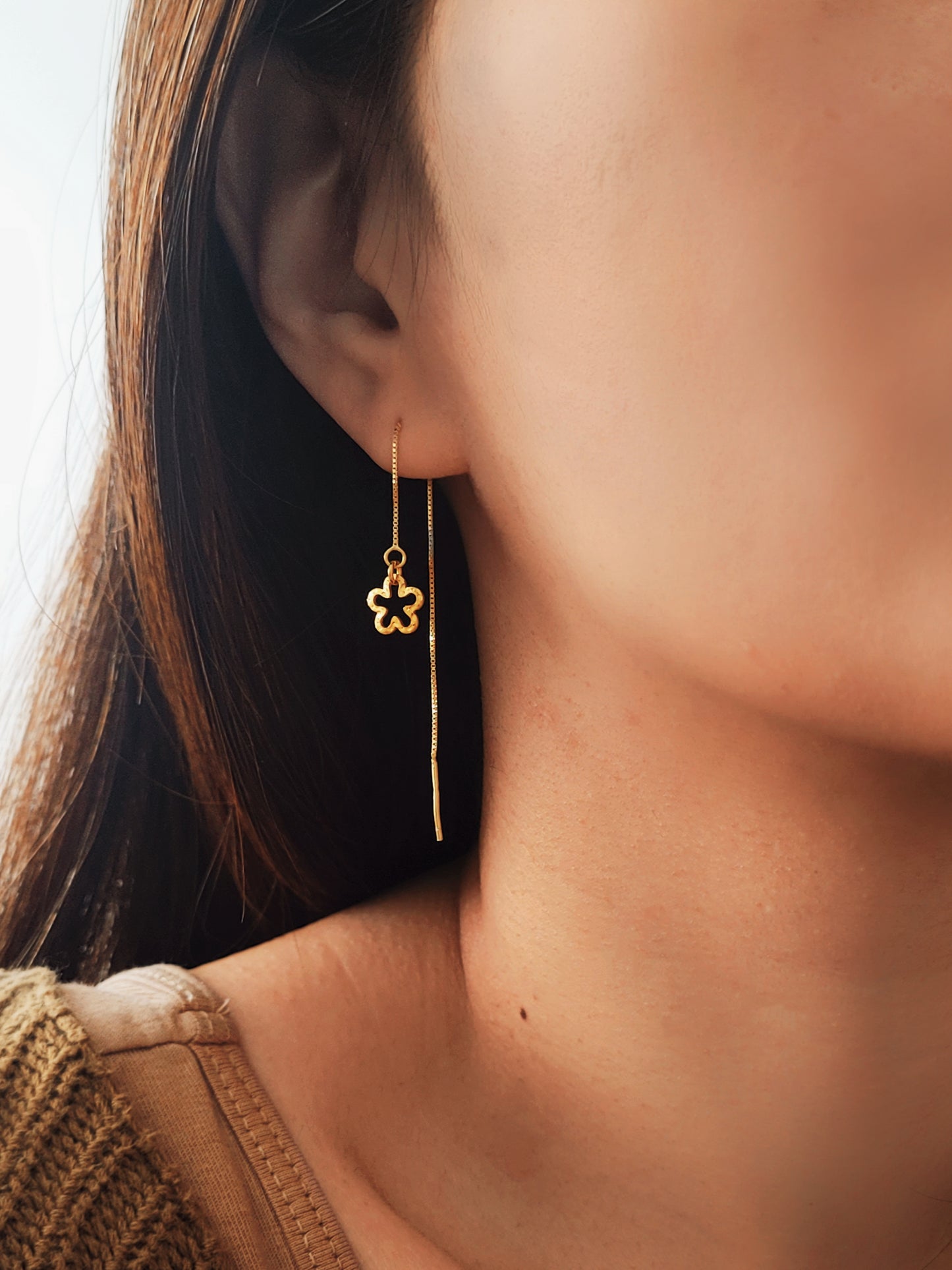 Close-up of a girl wearing a gold flower-shaped threader earring.