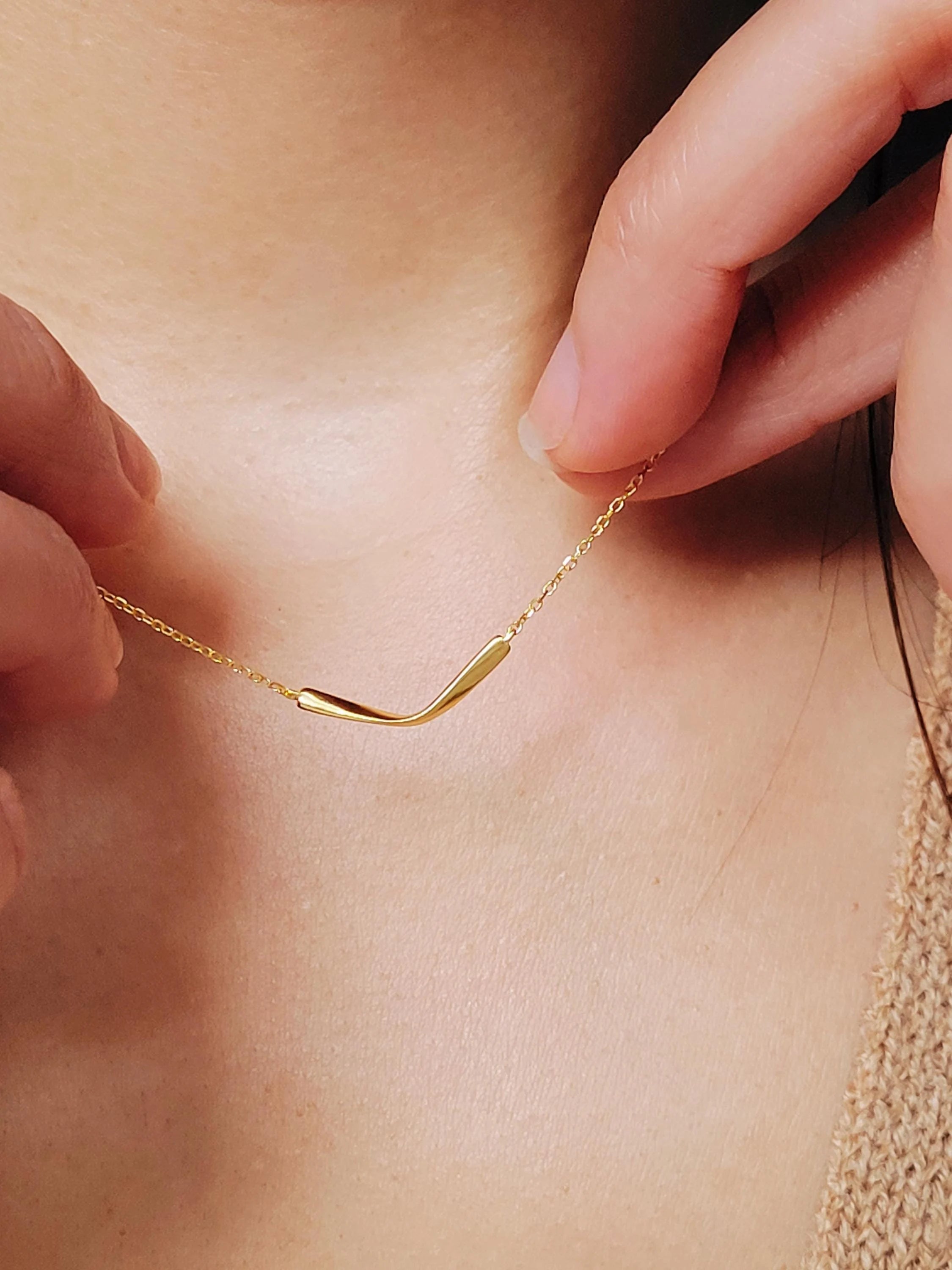 A delicate gold chain necklace with a simple, curved pendant crafted in gold plated sterling silver.