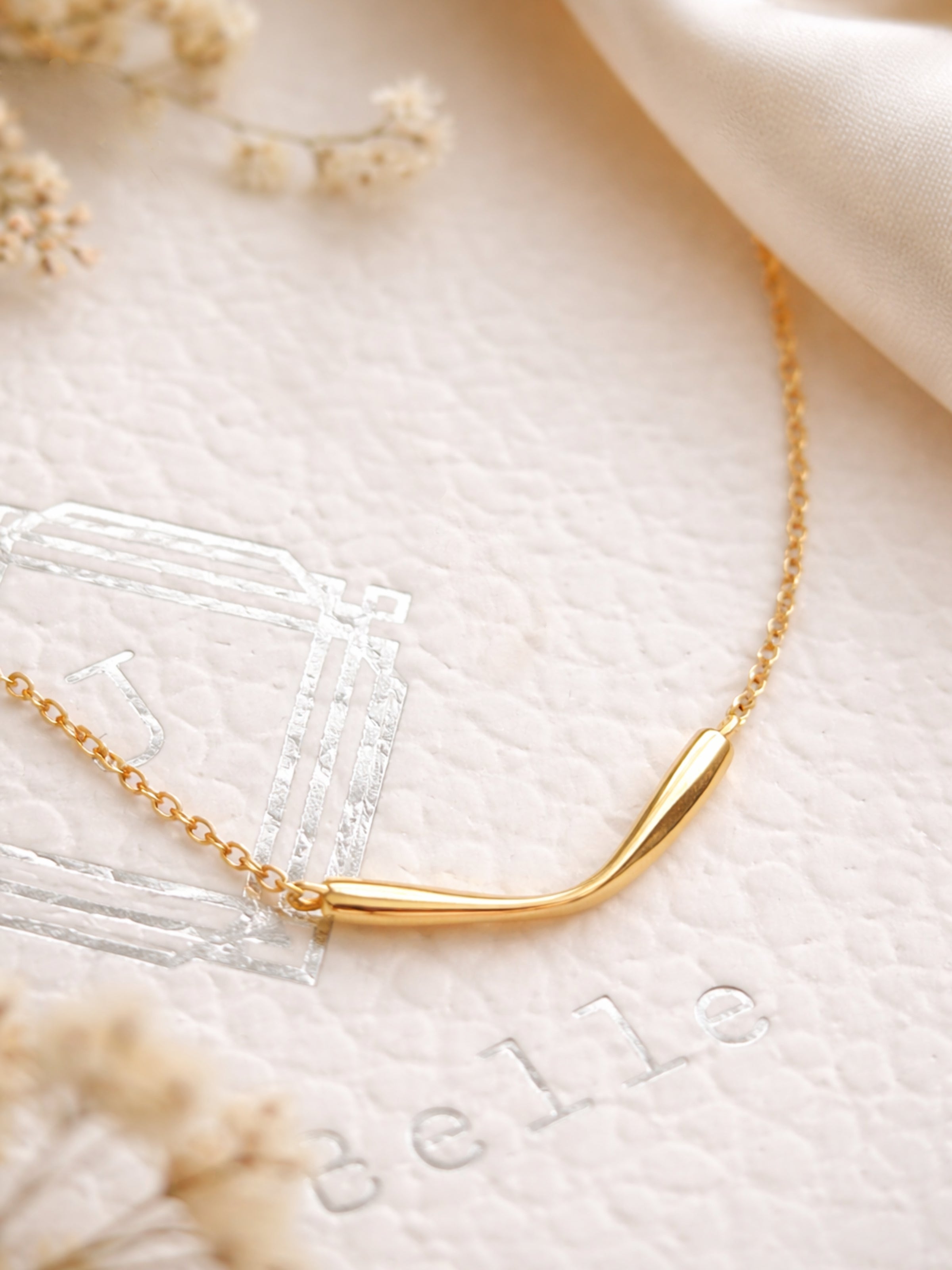 A minimalist gold bar necklace on a soft beige fabric background