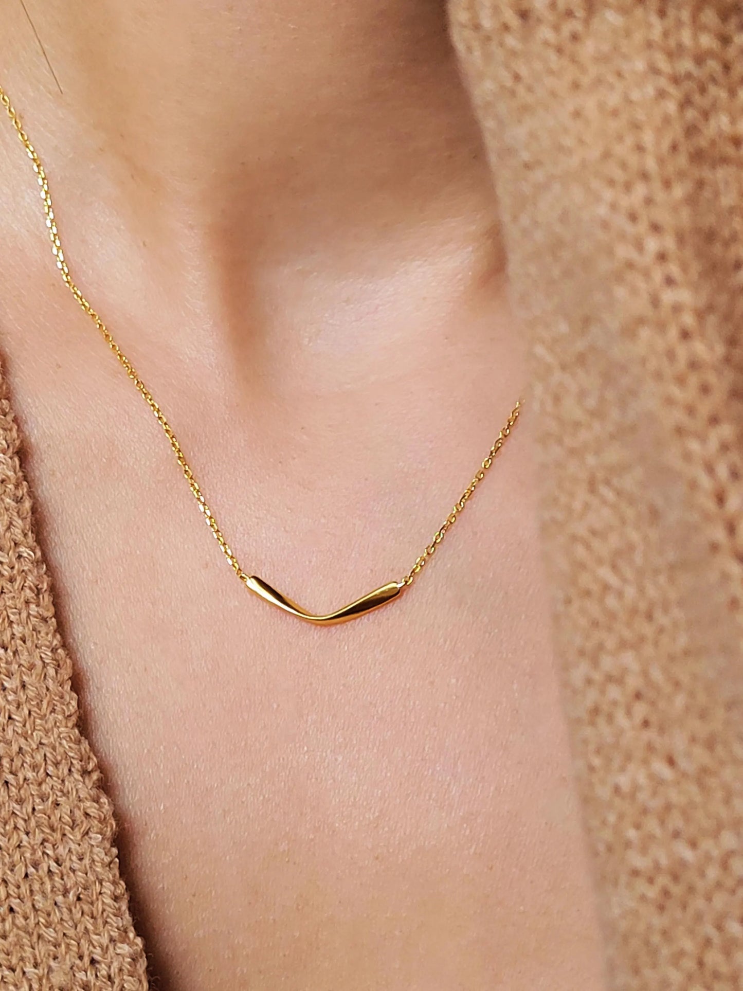 Close up of a woman wearing a simple gold curve bar necklace