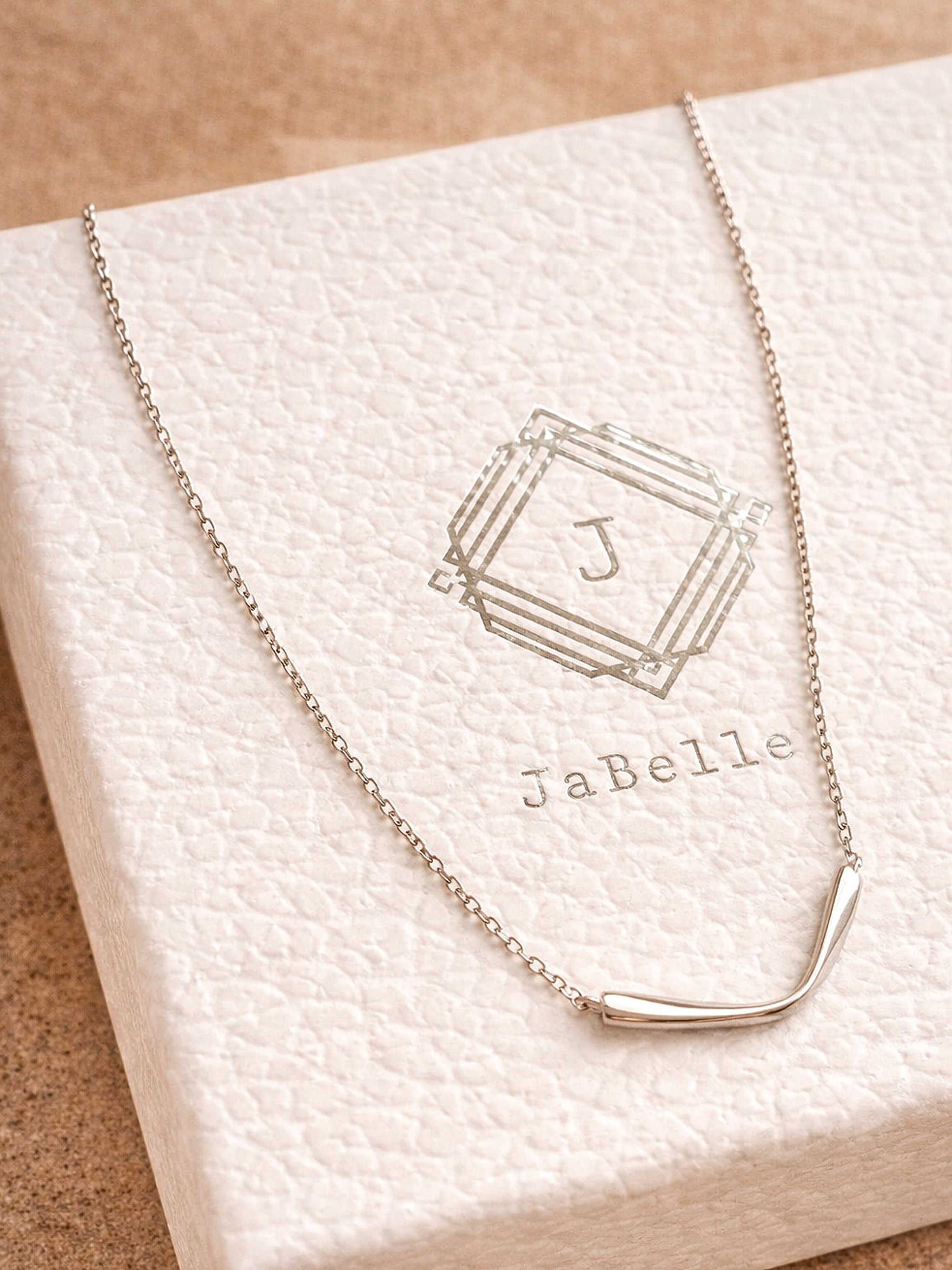 A simple sterling silver necklace with a v shape pendant on a white box