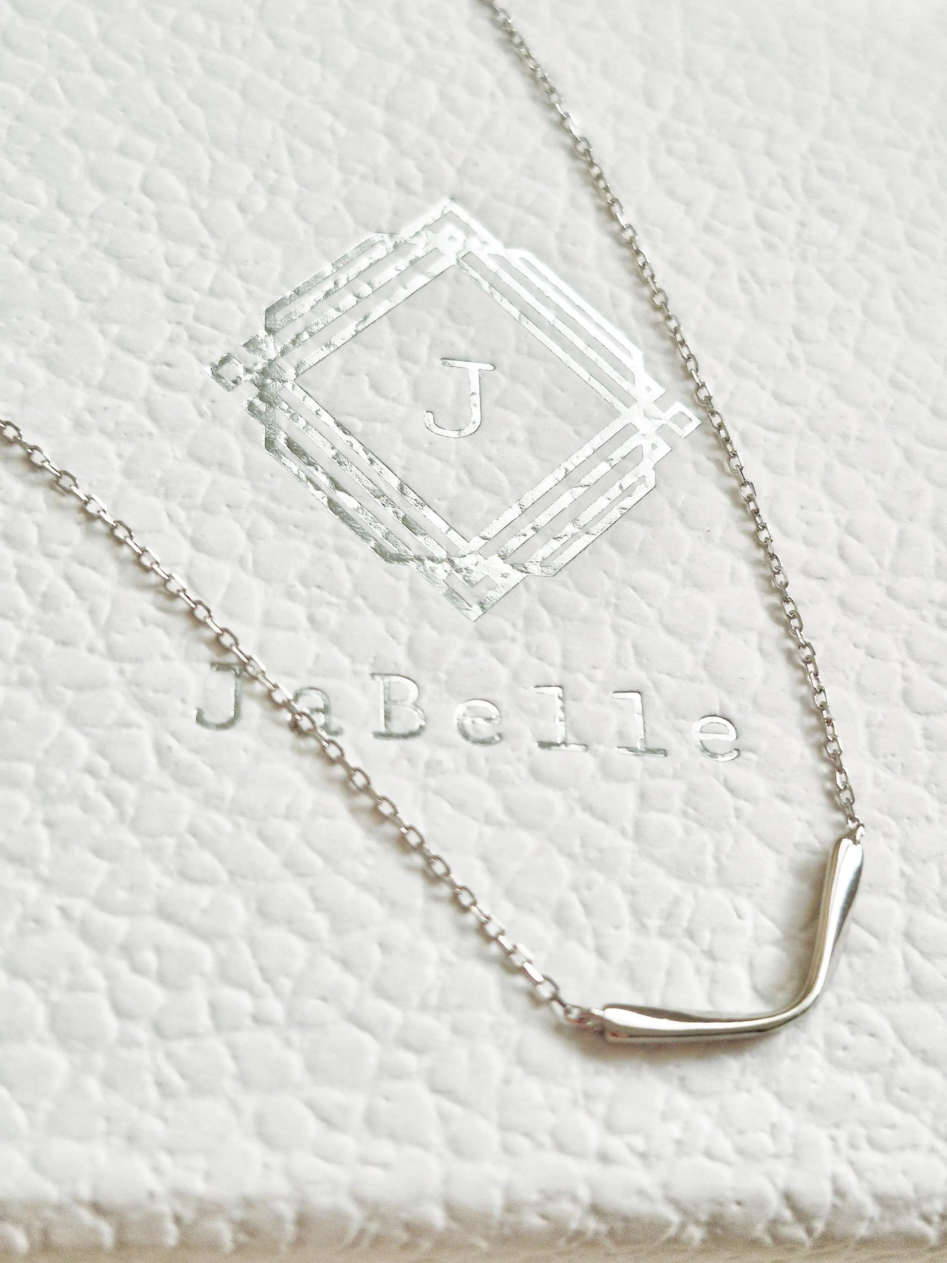 Close up of a dainty silver curve bar necklace crafted in 925 sterling silver displayed on a jewellery box