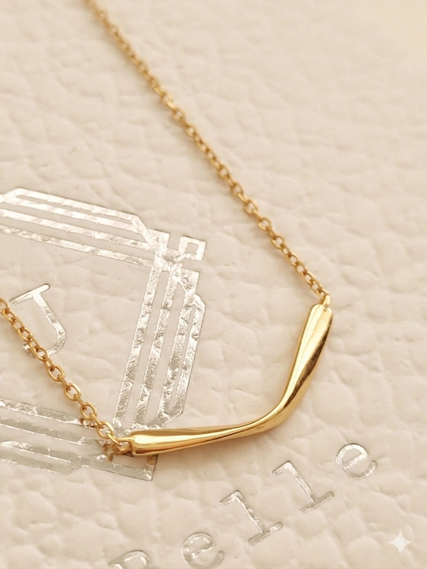 A minimalist gold necklace on a textured beige background