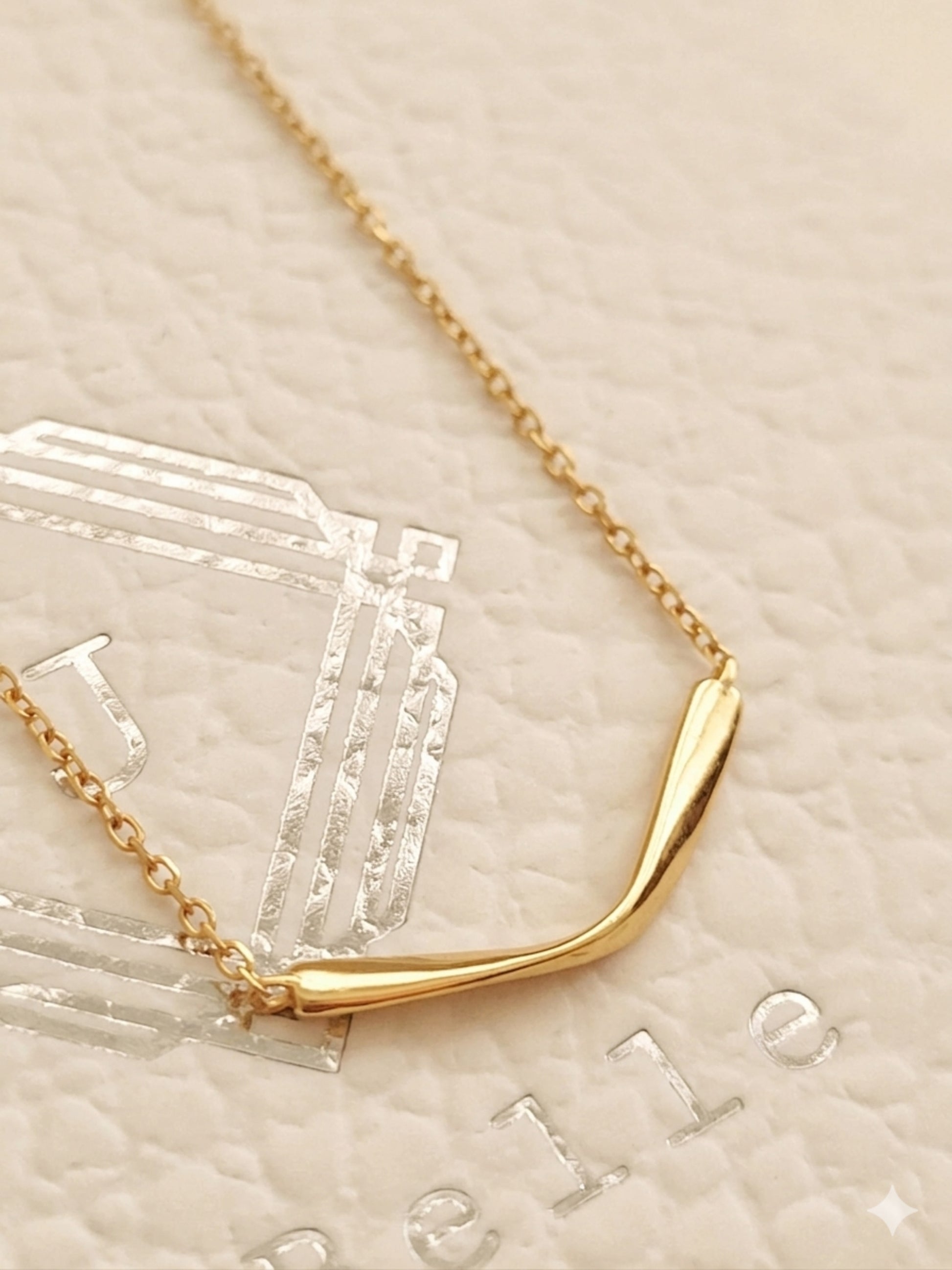 A minimalist gold necklace on a textured beige background