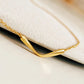 A gold necklace featuring a simple, curved pendant. The pendant is a single, smooth, curved line.