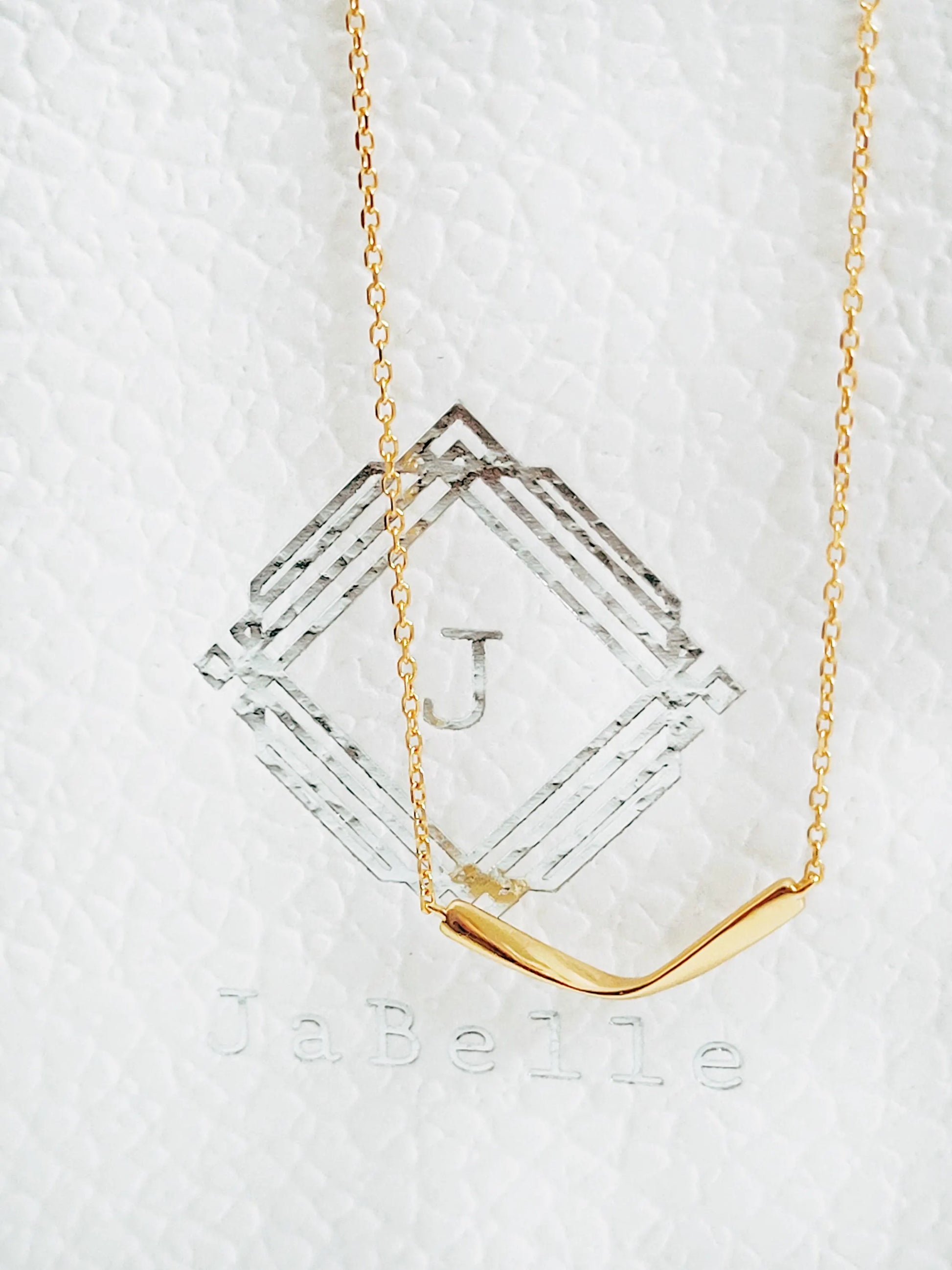 Close up of a simple curve bar necklace crafted in gold plated sterling silver on a JaBelle Jewellery box