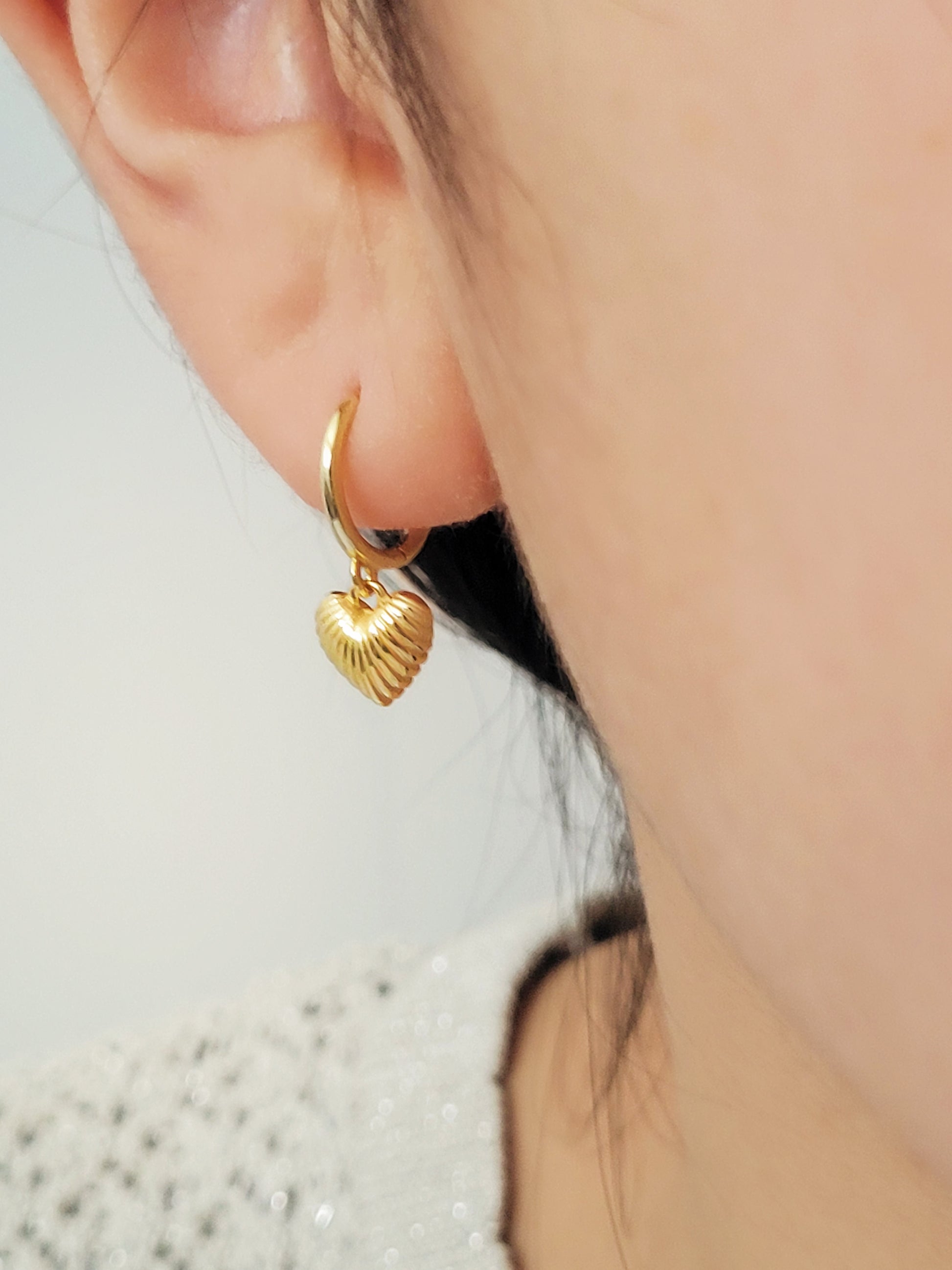 A woman wearing gold plated sterling silver heart dangle earrings. Simple, classic and minimalist design perfect for everyday wear.