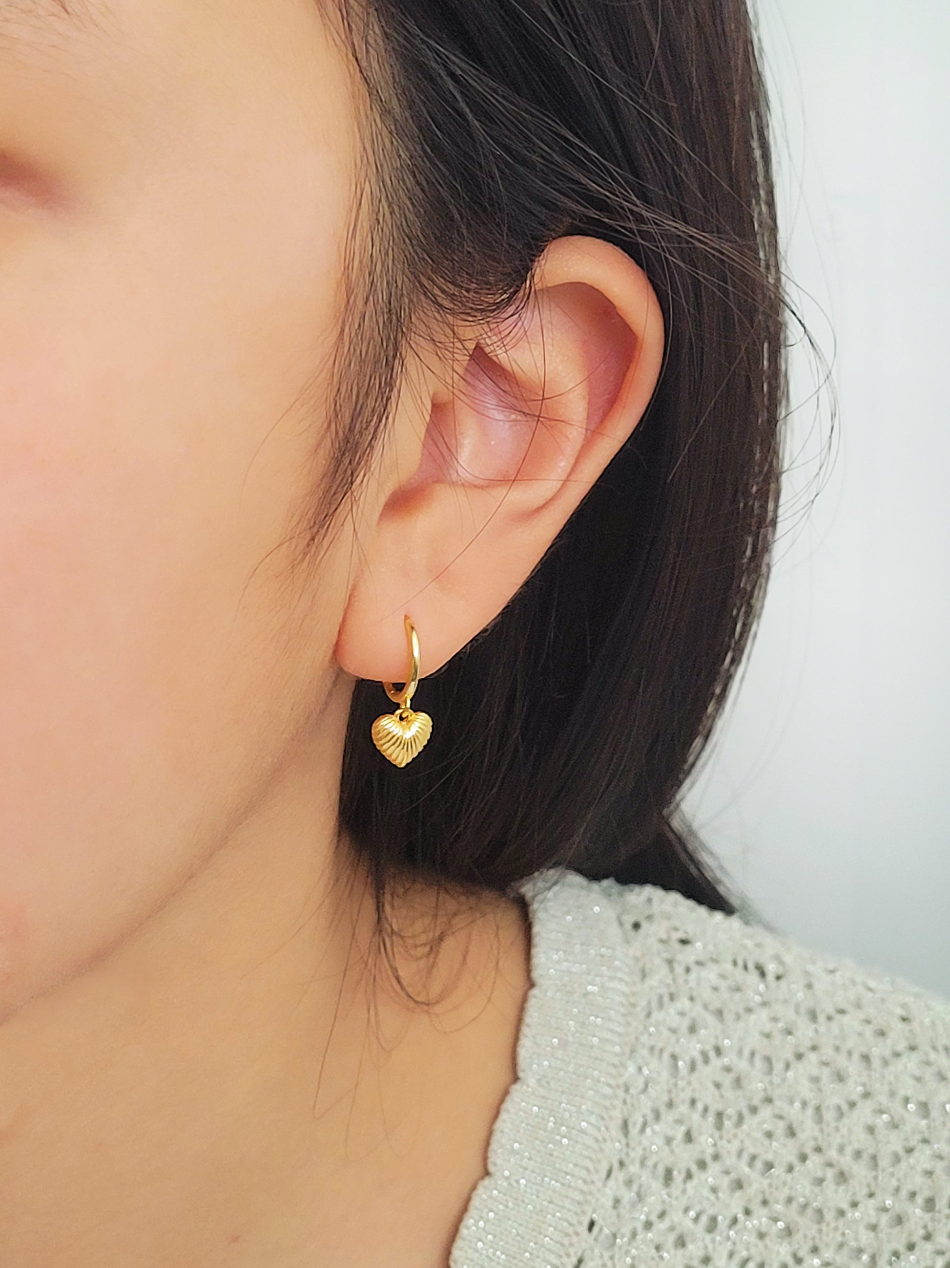 A woman wearing gold plated sterling silver heart dangle earrings. Simple, classic and minimalist design perfect for everyday wear.