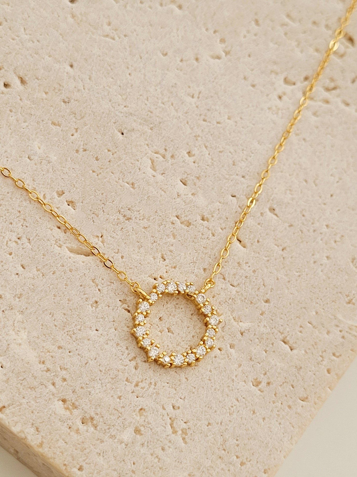 Close-up of Gold Vermeil Infinity Circle Necklace with pave zircon diamonds on a flat surface.