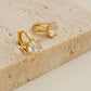 Close-up of a gold vermeil solitaire huggie earring with a large cubic zirconia stone displayed on a natural color stone board.