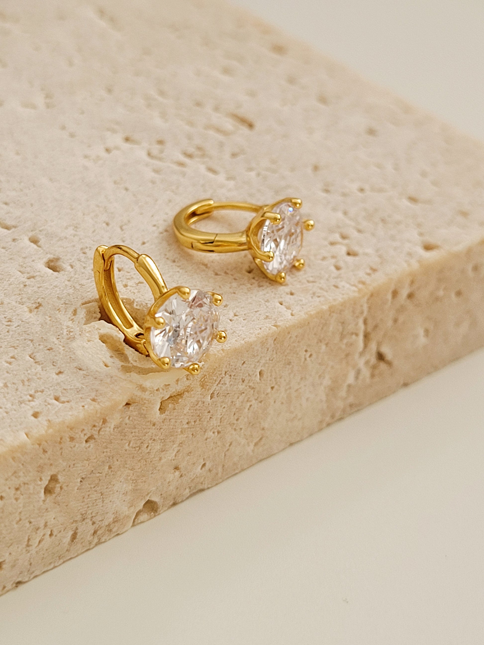 Close-up of a gold vermeil solitaire huggie earring with a large cubic zirconia stone displayed on a natural color stone board.