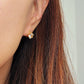 Minimalist gold huggie earrings with a large, clear cubic zirconia centerpiece shown on a model's ear.
