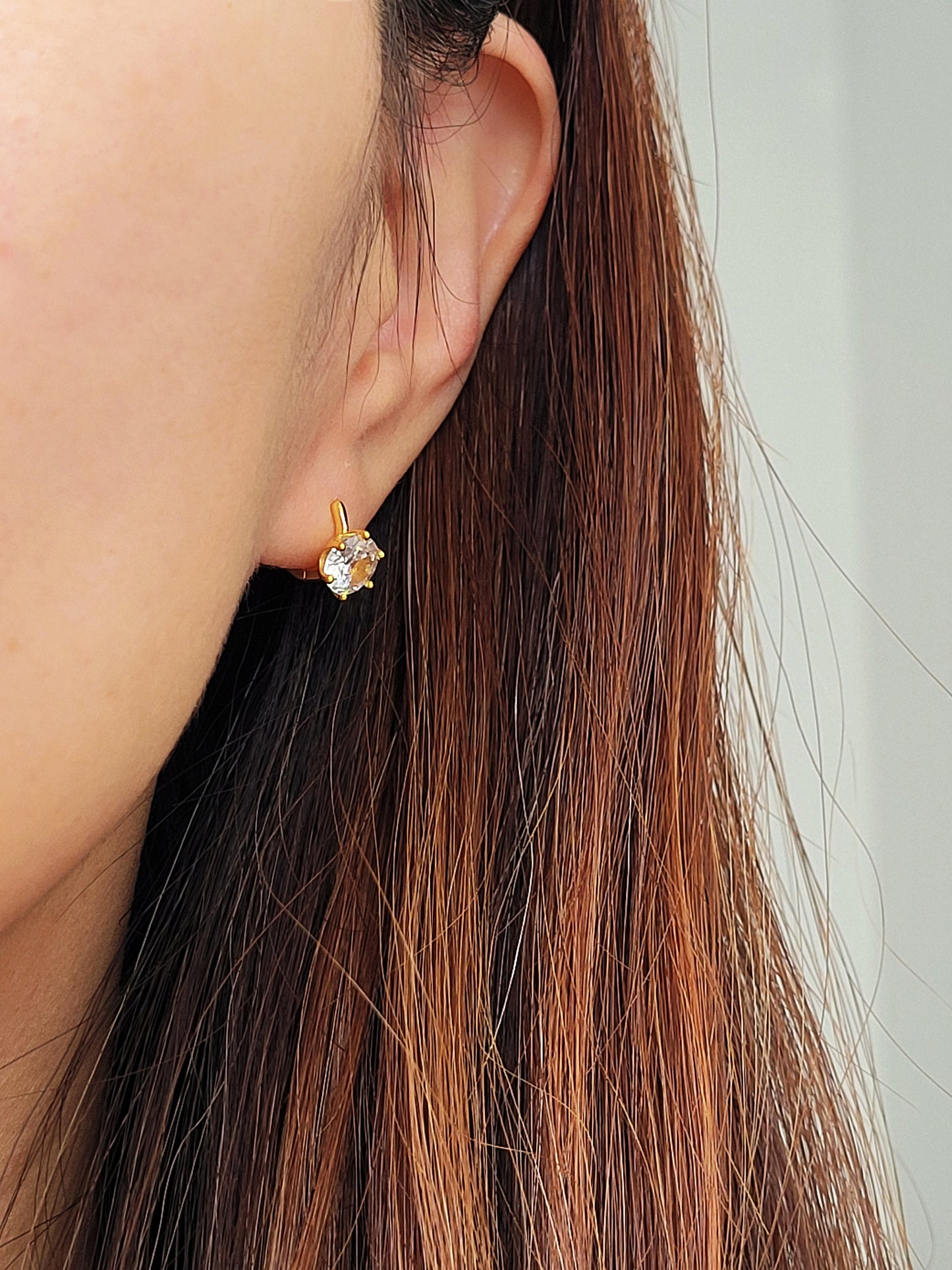 Minimalist gold huggie earrings with a large, clear cubic zirconia centerpiece shown on a model's ear.