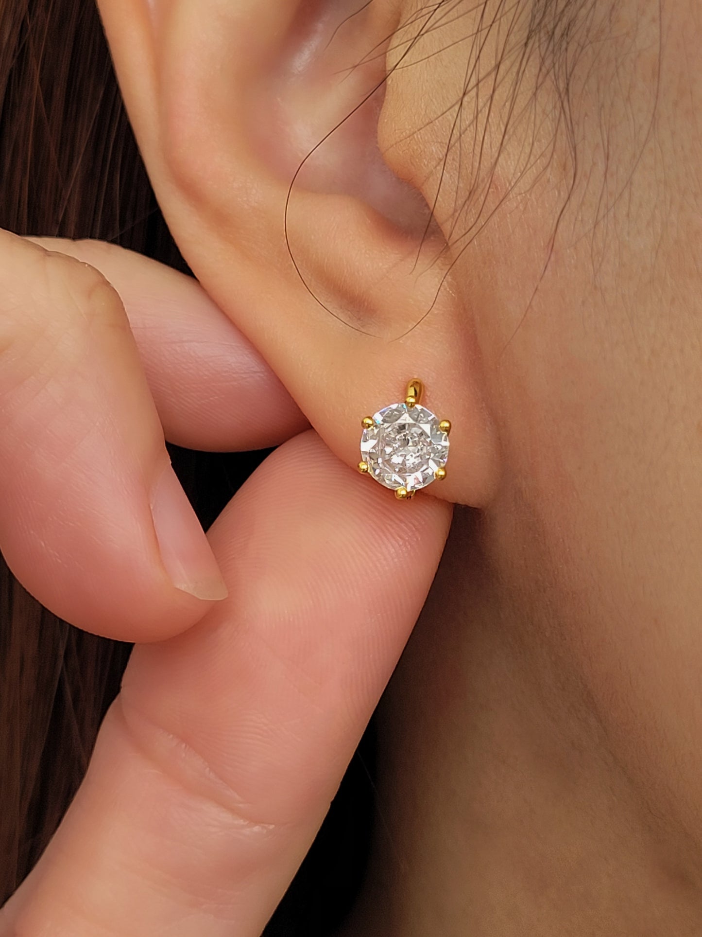 Close-up of a gold vermeil solitaire huggie earring with a large cubic zirconia stone worn on an ear