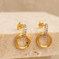 A pair of halo drop stud earrings in gold vermeil with cz diamond accents displayed on an esthetic beige color stone surface
