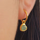Gold heart earring with a green gemstone worn by an ear