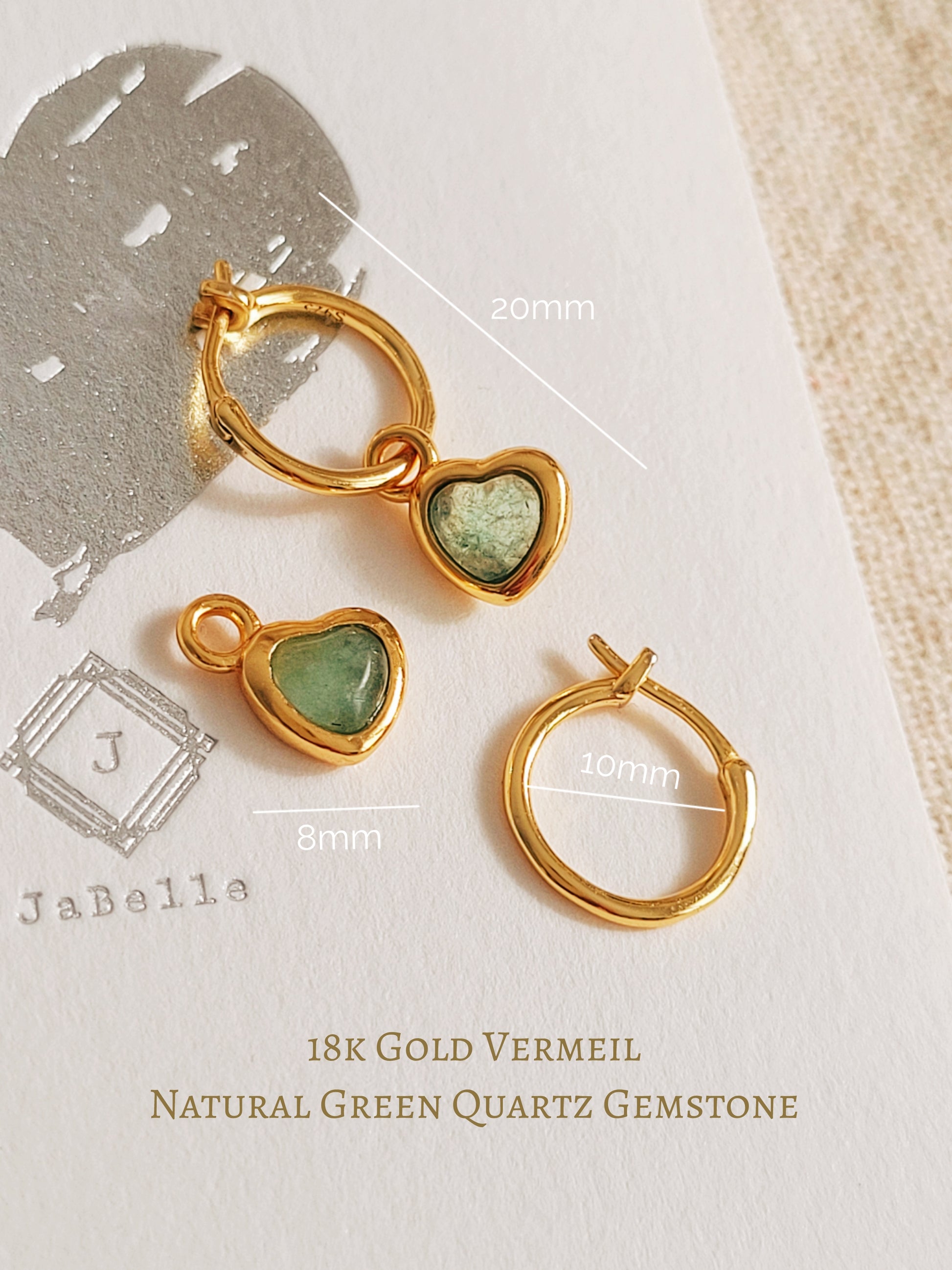 Gold hoop earrings with green crystal quartz on a textured surface
