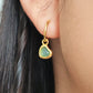 Gold heart dangle earring with a green gemstone worn by a person
