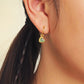 Cute gold heart earring with a green gemstone worn by a woman