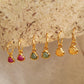 Set of gold heart earrings with gemstone drops on a textured beige background