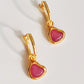 Gold heart earrings with pink gemstones on a light background