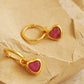 A pair of gold hoop earrings with heart dangle displayed on a stone surface