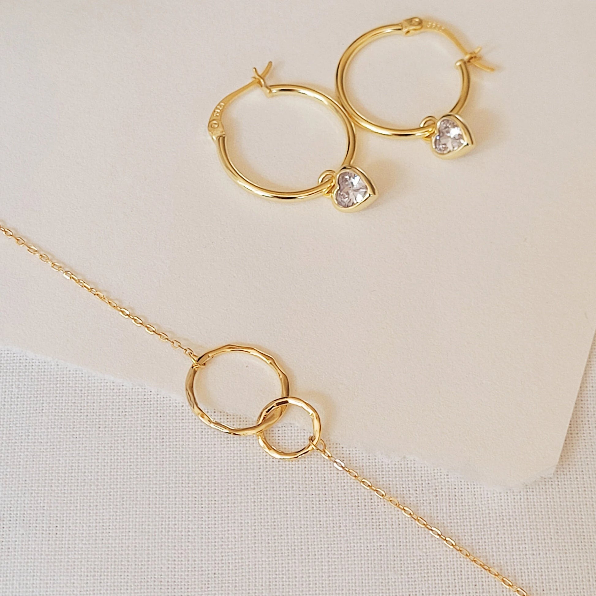 Gold-plated interlocking rings bracelet on a paper pair with minimalist crystal hoop earrings, ideal for modern jewelry lovers seeking a versatile and dainty accessory.